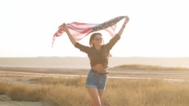 Mutlu bir kadın elinde bir Amerikan bayrağıyla yazın açık havada koşuyor.