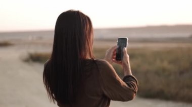 Yazın gün batımında manzaranın fotoğrafını çeken bir kadının yan görüntüsü.