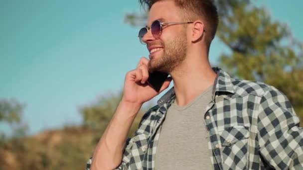 Een Glimlachende Man Met Een Zonnebril Praat Zijn Smartphone Terwijl — Stockvideo