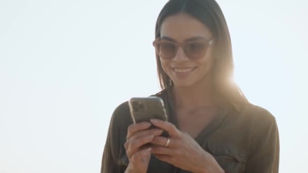 Улыбающаяся Женщина Солнечных Очках Пользуется Своим Мобильным Телефоном Стоя Улице — стоковое видео