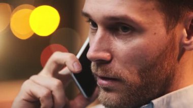 Yakışıklı sakallı bir adamın yakın plan görüntüsü akıllı telefonuyla konuşuyor.