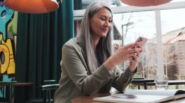 Gülümseyen bir kadın kafenin içinde akıllı telefonunu kullanıyor.