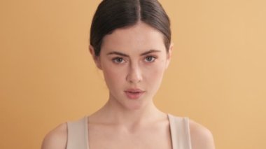 Çekici bir kadın kameraya poz veriyor. Stüdyodaki bej duvarın üzerinde tek başına duruyor.