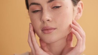 Güzel bir kadının yakın çekim görüntüsü kameraya poz veriyor. Stüdyodaki bej duvarın üzerinde izole bir şekilde duruyor.