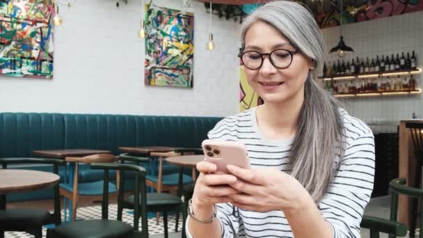 Leende Äldre Kvinna Använder Sin Mobil Sittandes Caféet Inuti — Stockvideo