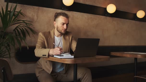 一位穿着夹克的英俊的白人商人在咖啡店的桌子旁使用笔记本电脑时 带着收据工作 — 图库视频影像