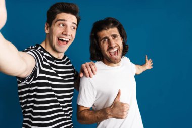 Beyaz, mavi arka planda izole edilmiş selfie çekerken baş parmağını kaldıran iki adamı heyecanlandırdı.