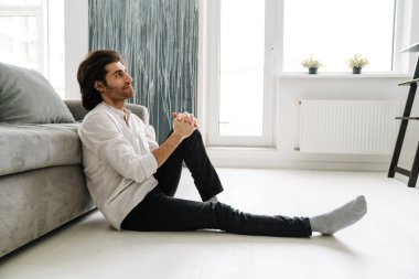 Orta yaşlı, esmer, Türk bir adam oturma odasında oturmuş televizyon seyrediyor.