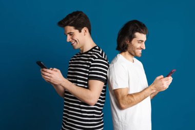 Beyaz mutlu iki adam mavi arka planda izole edilmiş cep telefonu kullanırken gülümsüyor