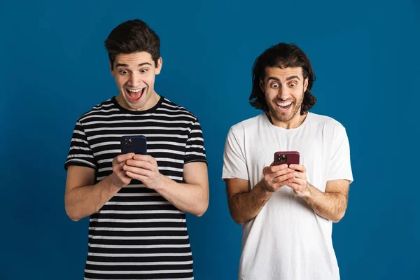 Spännande Två Män Skriker När Använder Mobiltelefoner Isolerade Över Blå — Stockfoto