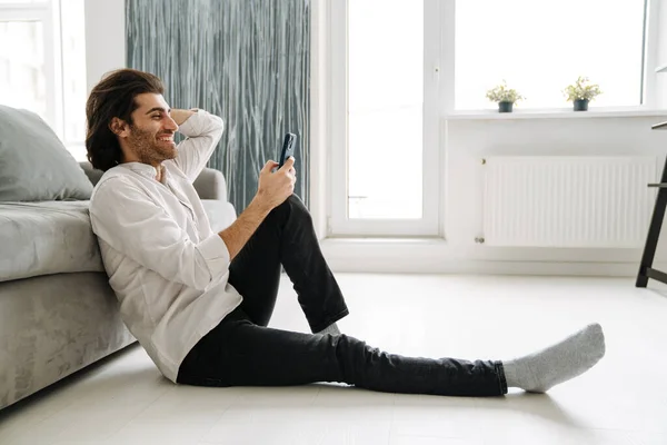 Sonriente Hombre Turco Mediana Edad Sosteniendo Teléfono Móvil Sentado Piso — Foto de Stock