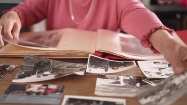 Yaşlı kadının, mutfakta bir fincan çay eşliğinde eski fotoğrafları albüme yerleştirdiği yakın plan bir görüntü.