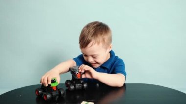 Mavi stüdyoda arabalarla oynayan, Down sendromlu gülümseyen küçük bir çocuk.