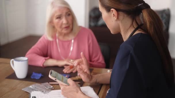 Вид Сбоку Врач Рассказывает Пожилой Пациентке Лечении Читая Телефону Кухне — стоковое видео