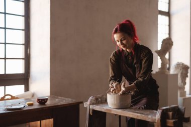 Genç, gülümseyen kadın heykeltıraş bir sanat stüdyosunda kille büst heykeli yapıyor.