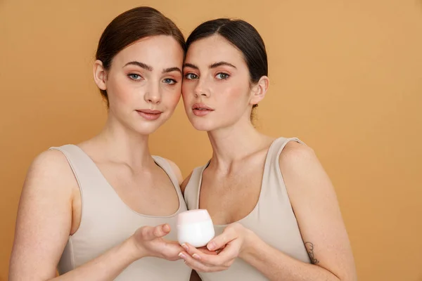 Jonge Twee Vrouwen Onderhemd Tonen Gezichtscrème Kijken Naar Camera Geïsoleerd — Stockfoto