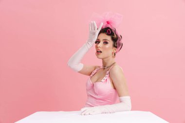 Genç, heyecanlı, pembe elbiseli beyaz kadın Barbie arka planda tek başına oturuyor.