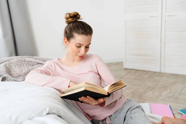 Молодая Улыбающаяся Белая Женщина Читает Книгу Сидя Полу Своей Спальни — стоковое фото