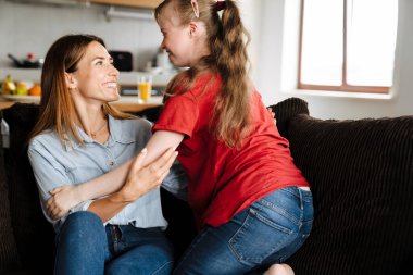 Down sendromlu bir kadın ve kızı evdeki kanepede otururken birbirlerine sarılıyorlar.