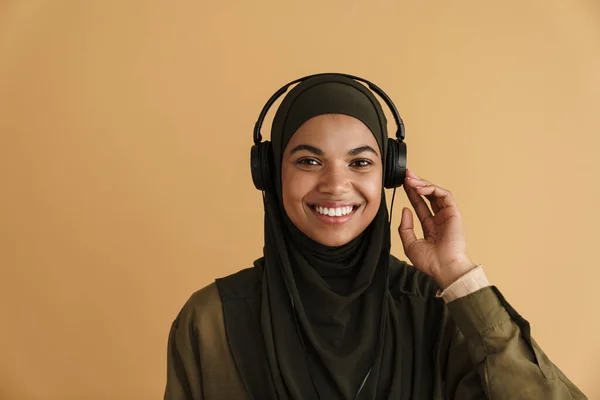 戴头巾听音乐的黑人穆斯林妇女 耳机与米色背景隔离 — 图库照片