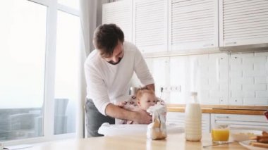 Yakışıklı bir baba evde kahvaltı ederken kızını çocuk sandalyesine oturtuyor.