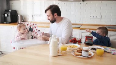 Bir baba, oğlu bir araba ile oynarken kahvaltıda küçük kızını besleyecek. Evde bebek bakıcılığı.