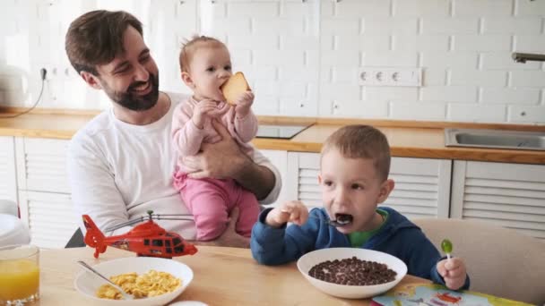 Padre Sonriente Sostiene Pequeña Hija Mientras Ella Está Comiendo Brindis — Vídeos de Stock