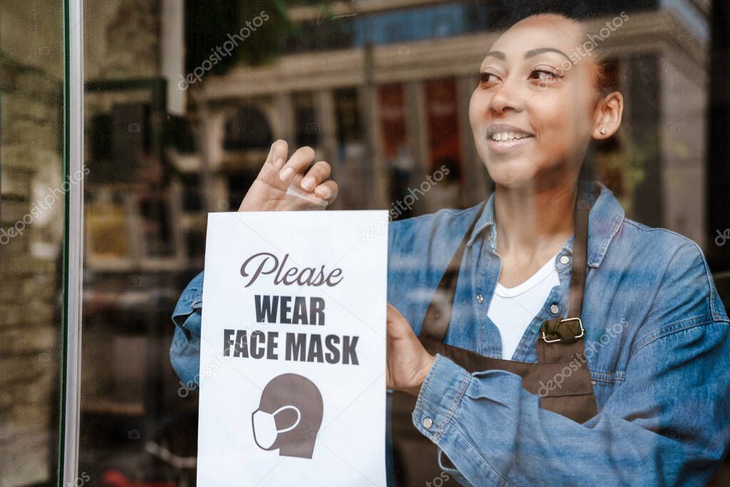 Black waitress sticking announce poster while working in cafe indoors