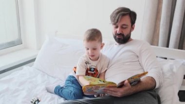 Yakışıklı bir baba oğluyla birlikte kitap okuyor.