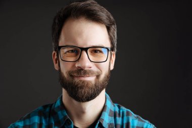 Gözlüklü mutlu adam, gülümsüyor ve siyah arka planda izole edilmiş kameraya bakıyor.