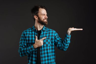 Tişörtlü, sakallı, gülümseyen adam siyah arka planda izole edilmiş telif alanını işaret ediyor.