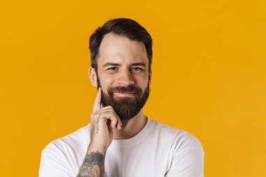 Gülümseyen esmer, sakallı adam sarı arka planda duran kameraya bakıyor.