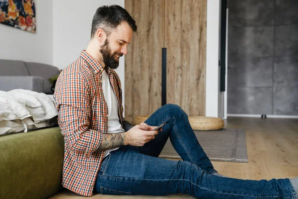 Sonriente Morena Mediana Edad Barbudo Hombre Sosteniendo Teléfono Móvil Sentado — Foto de Stock