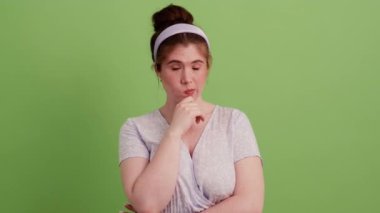 Kafasında çember olan ve yeşil bir stüdyoda omuzlarını silken, meditasyon yapan kızıl saçlı bir kız.