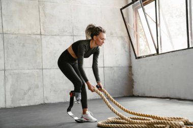 Protezli genç sporcu kadın savaş halatlarıyla içeride çalışıyor.