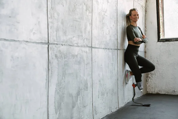 Joven Deportista Con Prótesis Sonriendo Mientras Apoya Pared Interior — Foto de Stock