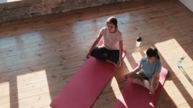 Kendine güvenen bir yoga eğitmeni yoga egzersizi yapıyor. Yoga stüdyosundaki yoga minderinde oturan Down sendromlu müşterisiyle birlikte.