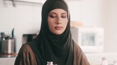 Yoğunlaştırılmış ciddi bir Arap kadın çöpleri ayırırken cam şişeleri konteynıra koyuyor.