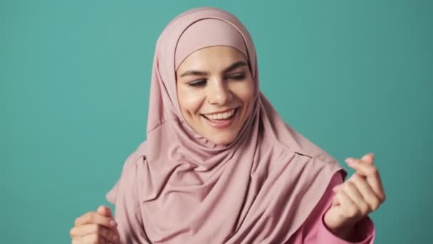 一个快乐的阿拉伯女人穿着粉色的民族头巾 在一个被蓝色背景隔开的工作室里跳舞 — 图库视频影像