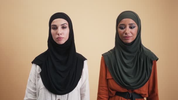 两名头戴头巾的困惑的阿拉伯妇女站在因米黄色背景而被隔离的工作室里做着脸 掌手势 — 图库视频影像