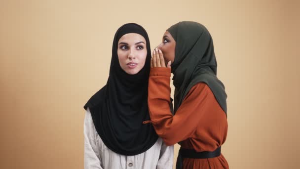 一位高兴的阿拉伯女人带着国徽 与她的朋友分享秘密 她站在一间因米色背景而与世隔绝的工作室里 — 图库视频影像