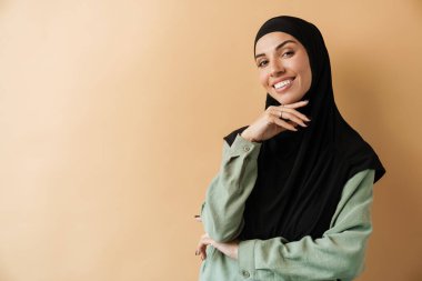 Bej arka planda duran tesettürlü gülümseyen müslüman bir kadının portresi