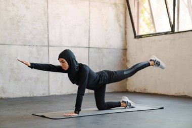 İçeride çalışırken tesettürlü genç müslüman kadın egzersiz yapıyor.