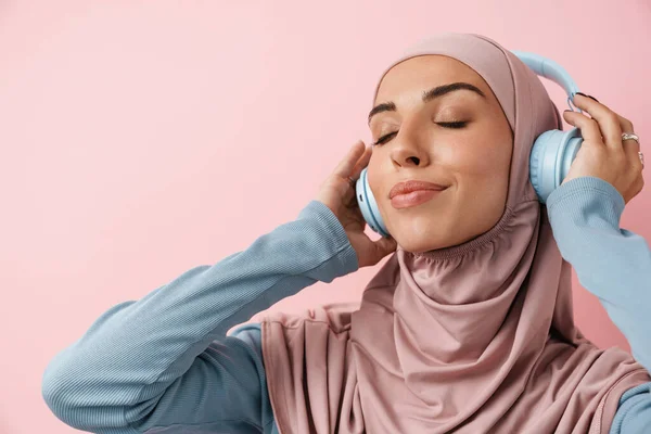 Positiivisen Musliminaisen Muotokuva Vaaleanpunaisissa Hijabeissa Musiikin Kuuntelemisessa Seistessään Vaaleanpunaisessa Studiossa — kuvapankkivalokuva