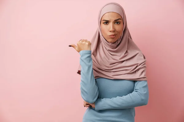 Muzułmanka Różowym Hidżabie Wskazująca Przestrzeń Marszcząca Czoło Różowym Studiu — Zdjęcie stockowe