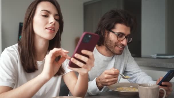 Uśmiechnięta Para Mężczyzna Kobieta Ogląda Coś Przez Komórkę Jedząc Śniadanie — Wideo stockowe