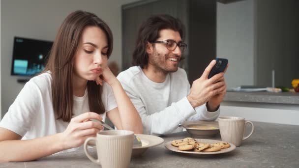 Niezadowolona Kobieta Śniadanie Podczas Gdy Jej Chłopak Siedzi Używa Telefonu — Wideo stockowe