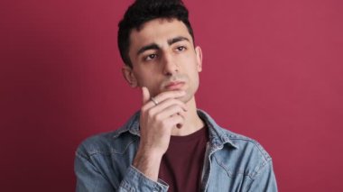 Ciddi bir esmer adam stüdyoda kırmızı arka planda izole edilmiş bir şey düşünüyor.