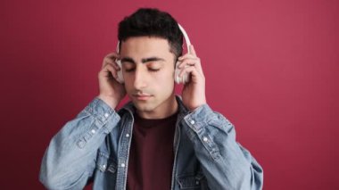 Yakışıklı, esmer bir adam müzik dinlerken stüdyoda kırmızı arka planda izole edilmiş kulaklıklar takıyor.