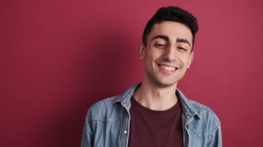 Gülümseyen esmer bir adam stüdyoda kırmızı arka planda tek başına duruyor.